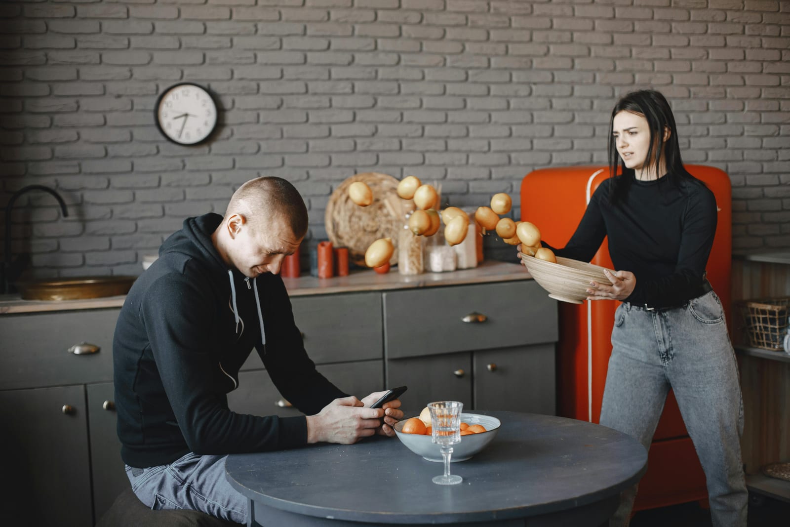 Žena v kuchyni vzteky odhazuje mísu s citrony, muž sedí u stolu a kouká do mobilu