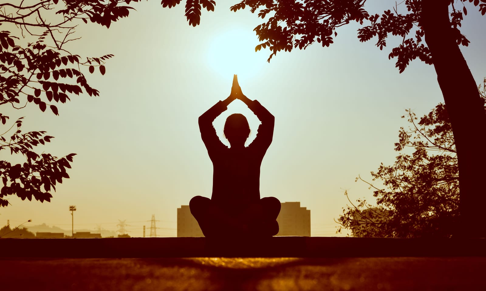 Silueta sedící osoby v meditaci s výhledem na západ slunce, klidná atmosféra