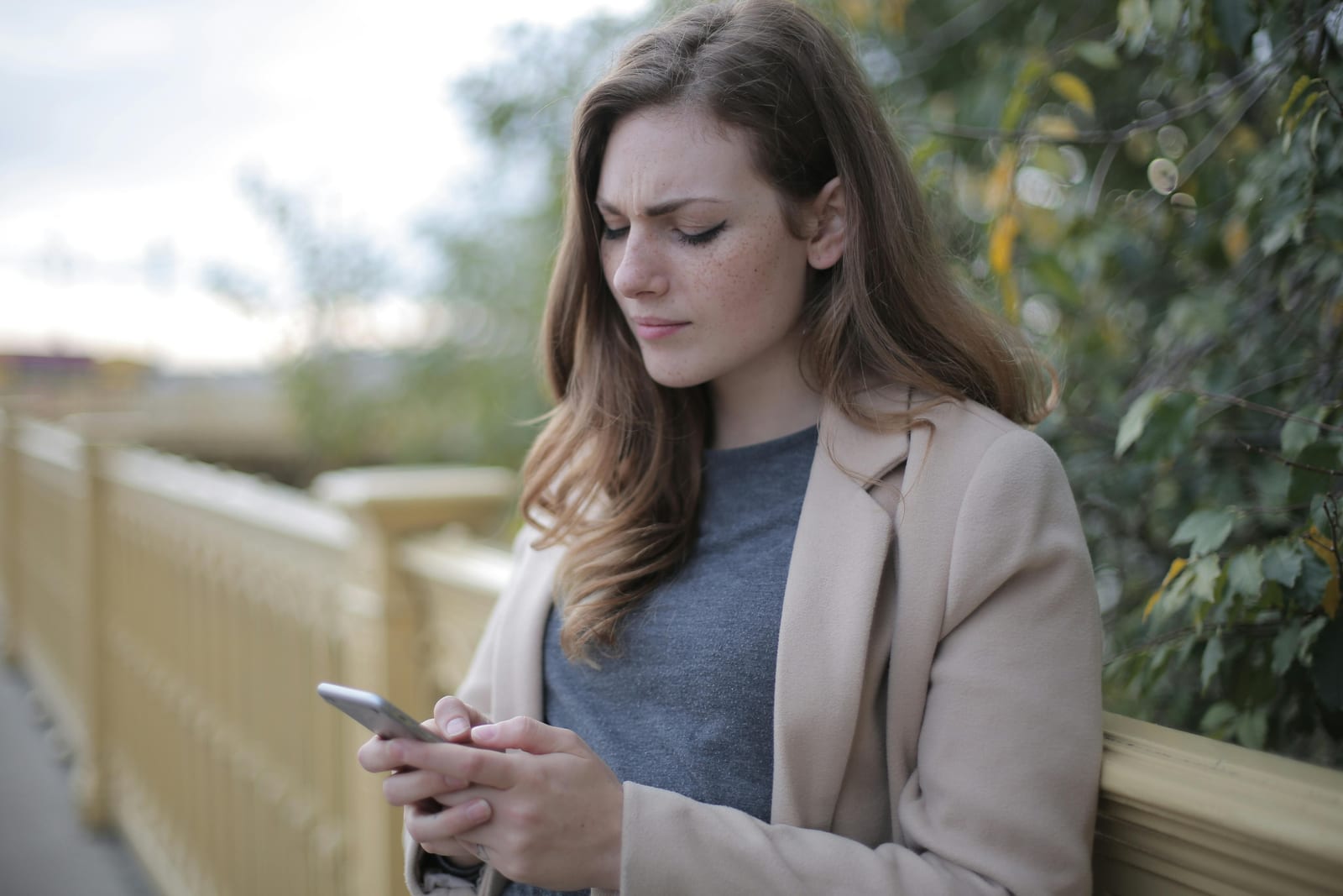 Žena venku se zamračeně dívá do mobilu