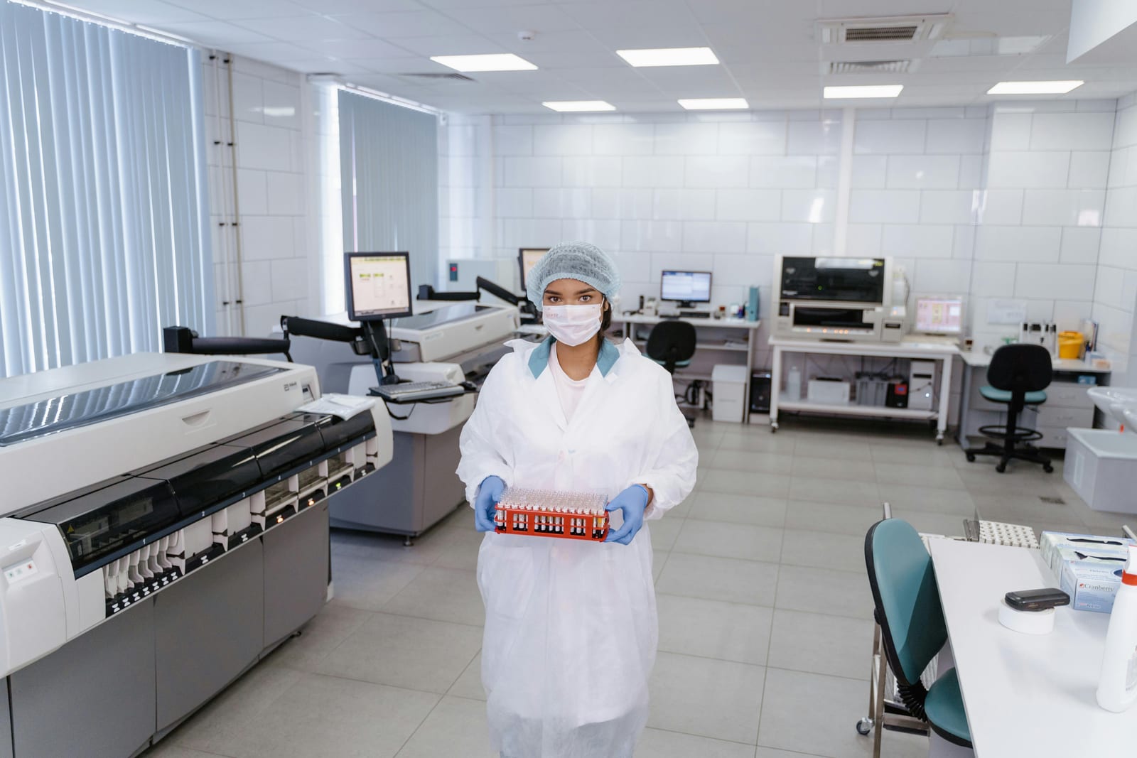 Laborantka v ochranném oděvu drží zkumavky se vzorky krve