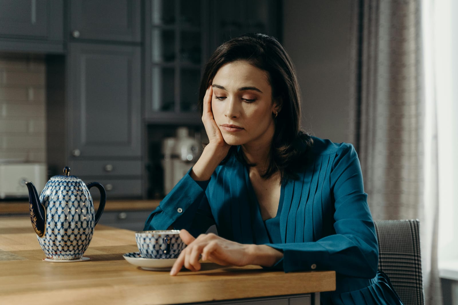 Žena sedí sama u kuchyňského stolu s šálkem a přemýšlí