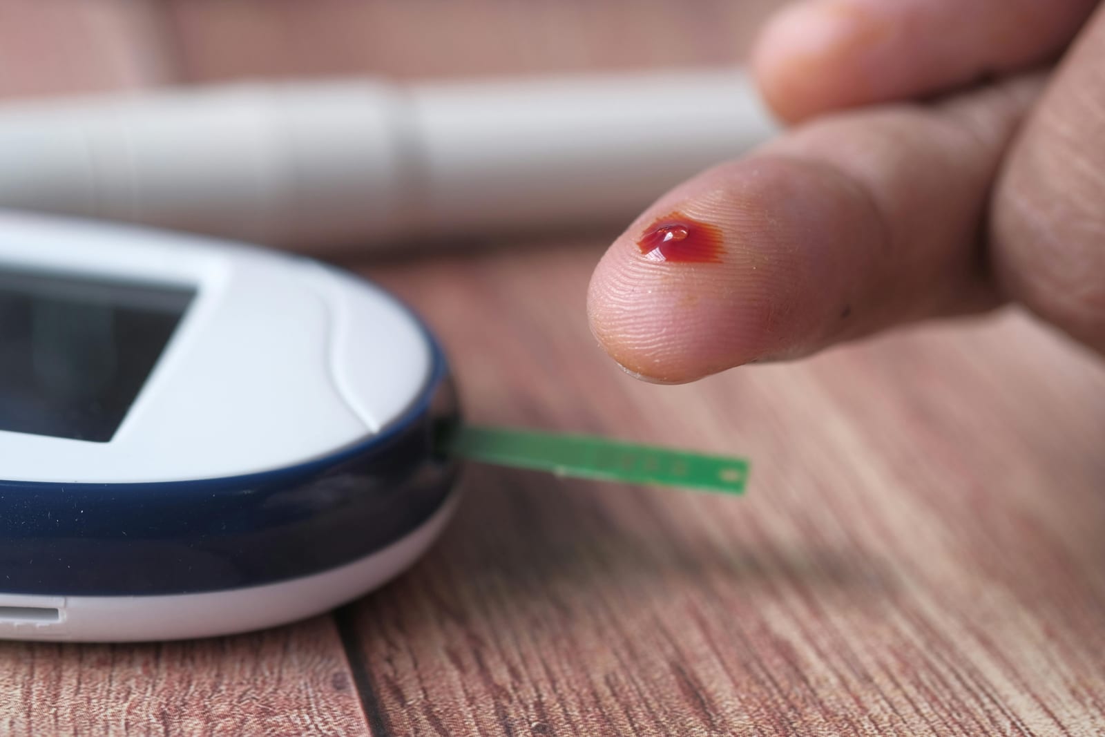 Detail prstu s kapkou krve a testovacího proužku zasunutého do glukometru