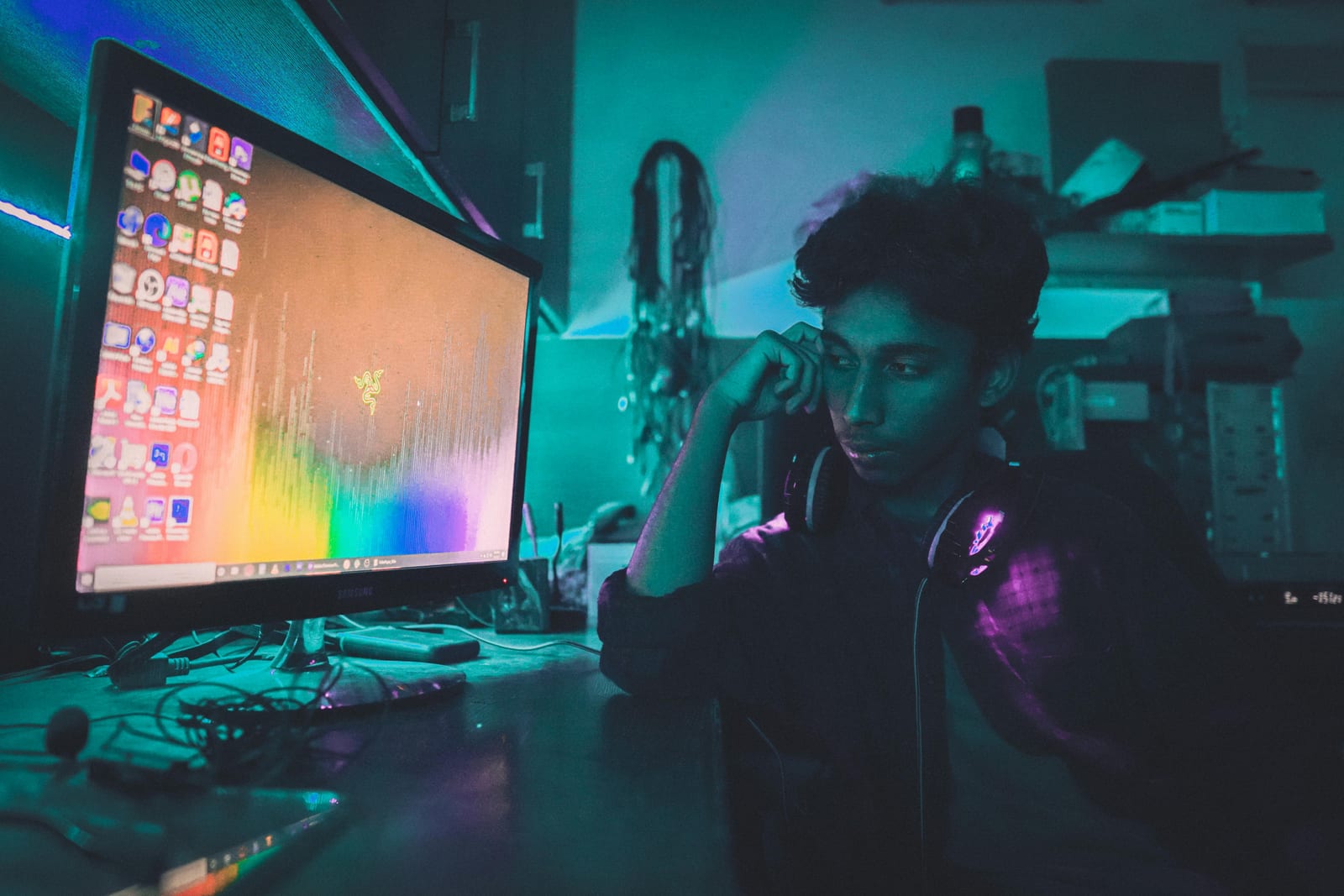 Mladý muž v noční místnosti s neonovým osvětlením, opřený o ruku, hledí do monitoru