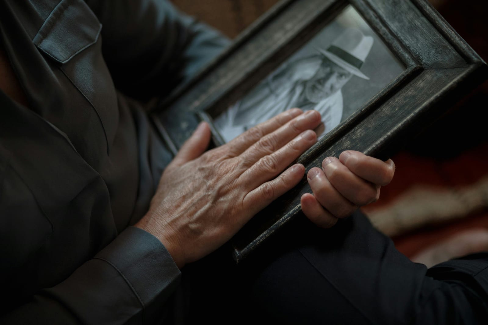 Detail starých rukou držících rámeček s fotografií, gesto vzpomínky