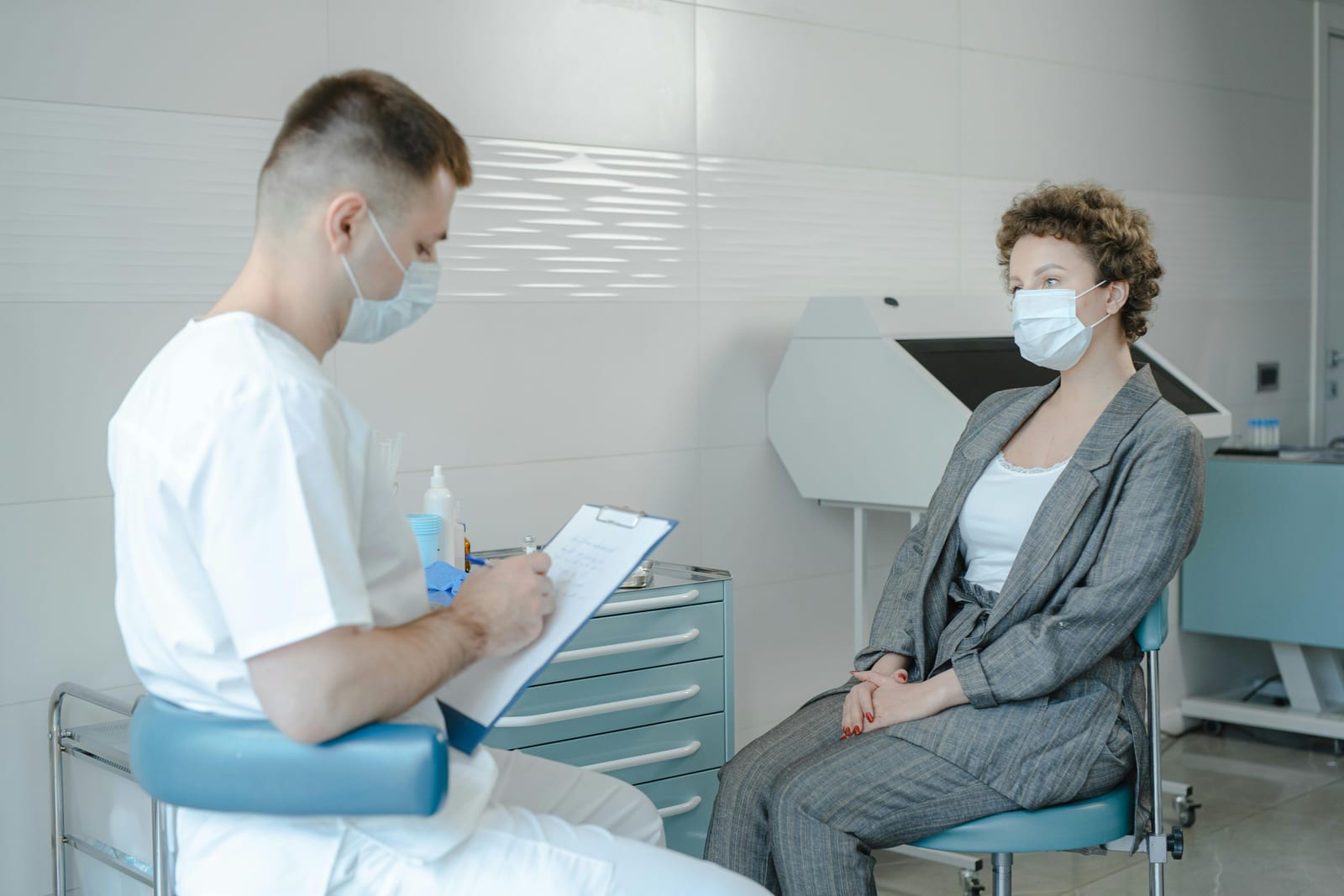 Lékař v ordinaci zapisuje informace, pacientka sedí naproti, neutrální klinické prostředí