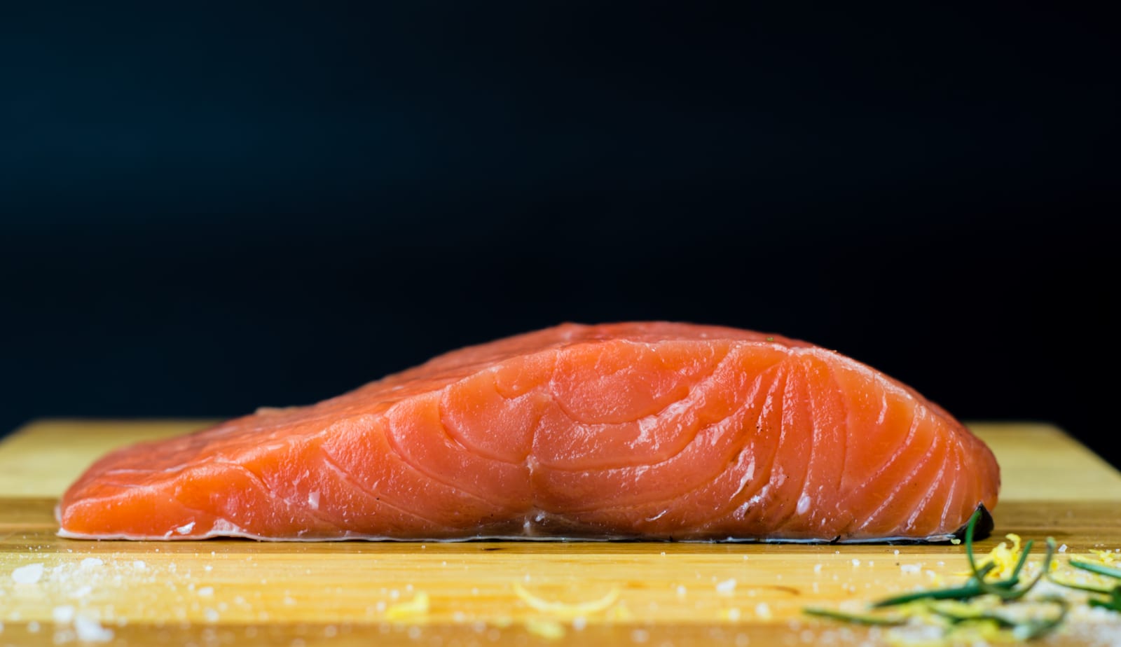 Filet syrového lososa na dřevěné desce, kolem sůl a citronová kůra