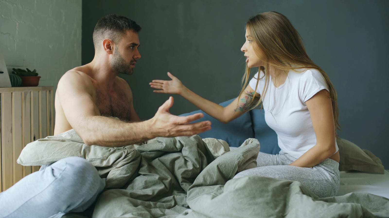 Pár sedí v posteli zády k sobě, obtížná konverzace, ranní světlo