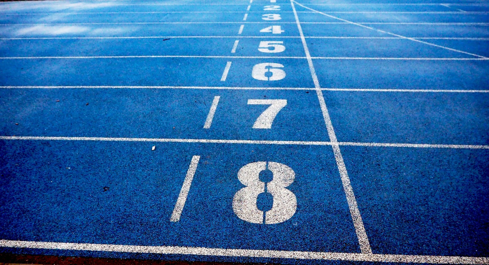 Prázdná modrá atletická dráha s čísly drah 2 až 8 na startovní čáře