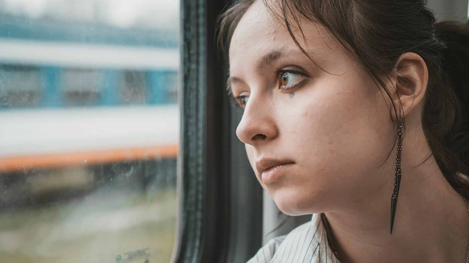 Dospívající dívka se zamyšleně dívá z okna vlaku