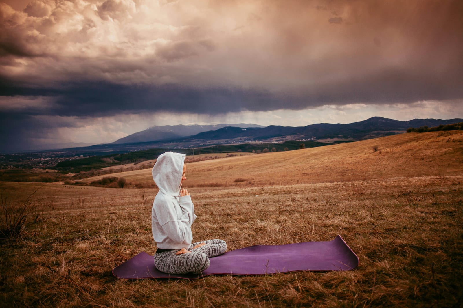 Osoba sedící v meditační pozici na trávě, modlitební korálky v ruce
