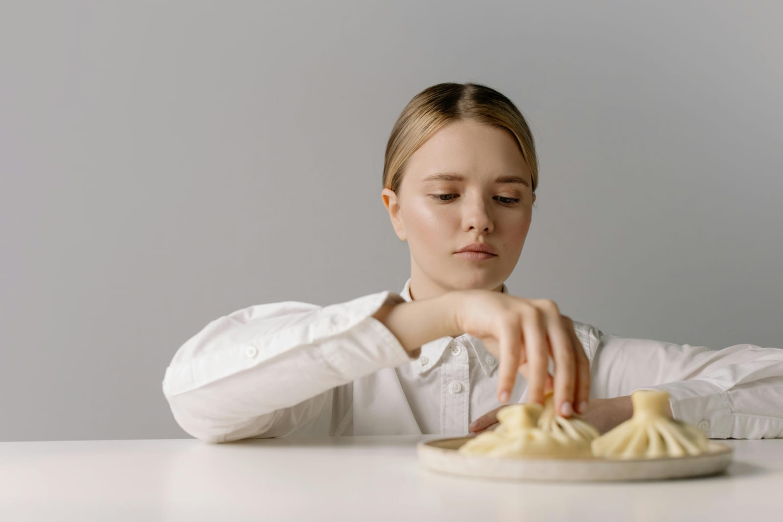 Žena u stolu nedůvěřivě sahá po jídle na talíři