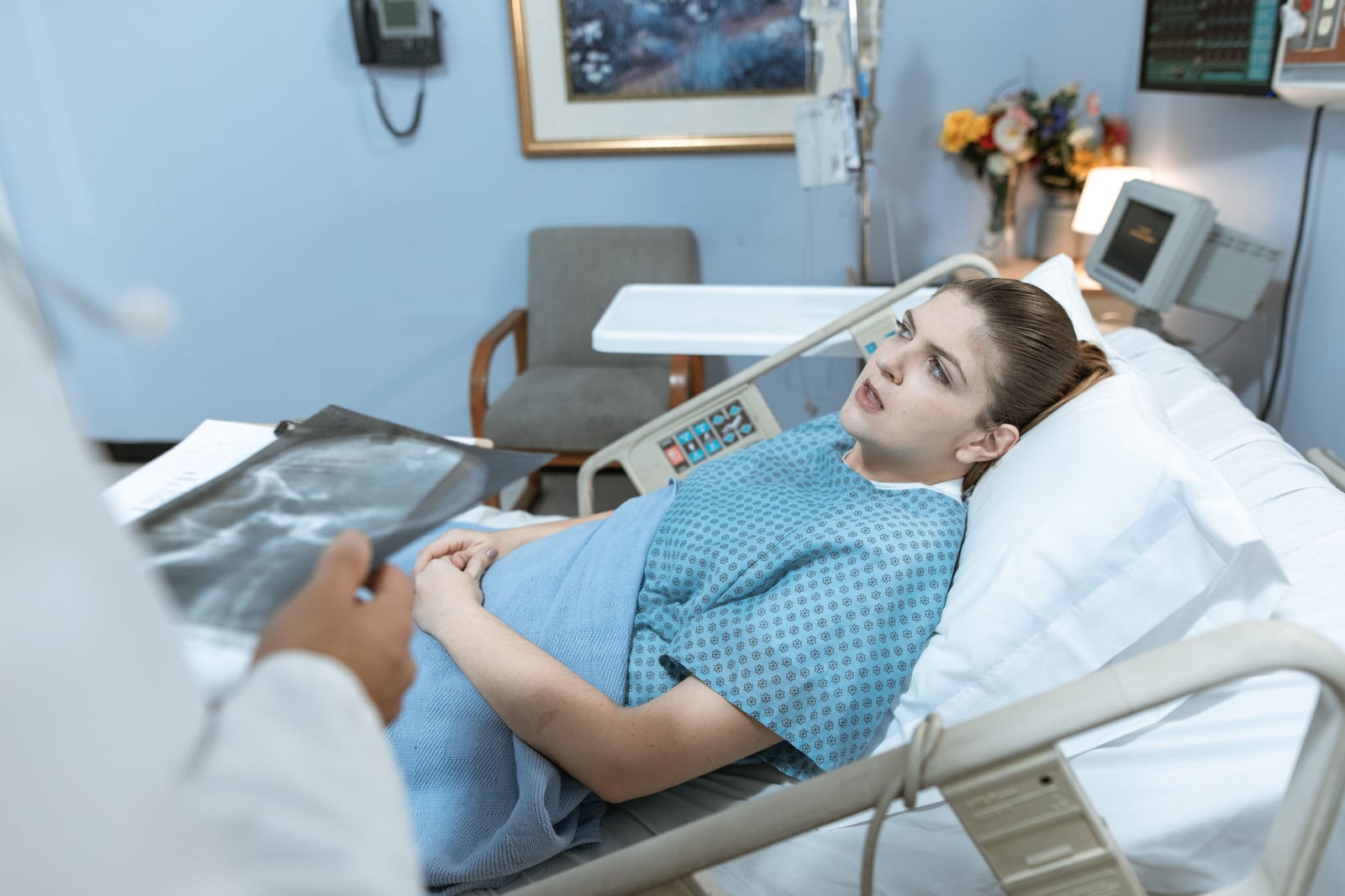 Mladá žena leží v nemocniční posteli a poslouchá lékaře, civilní nemocniční prostředí