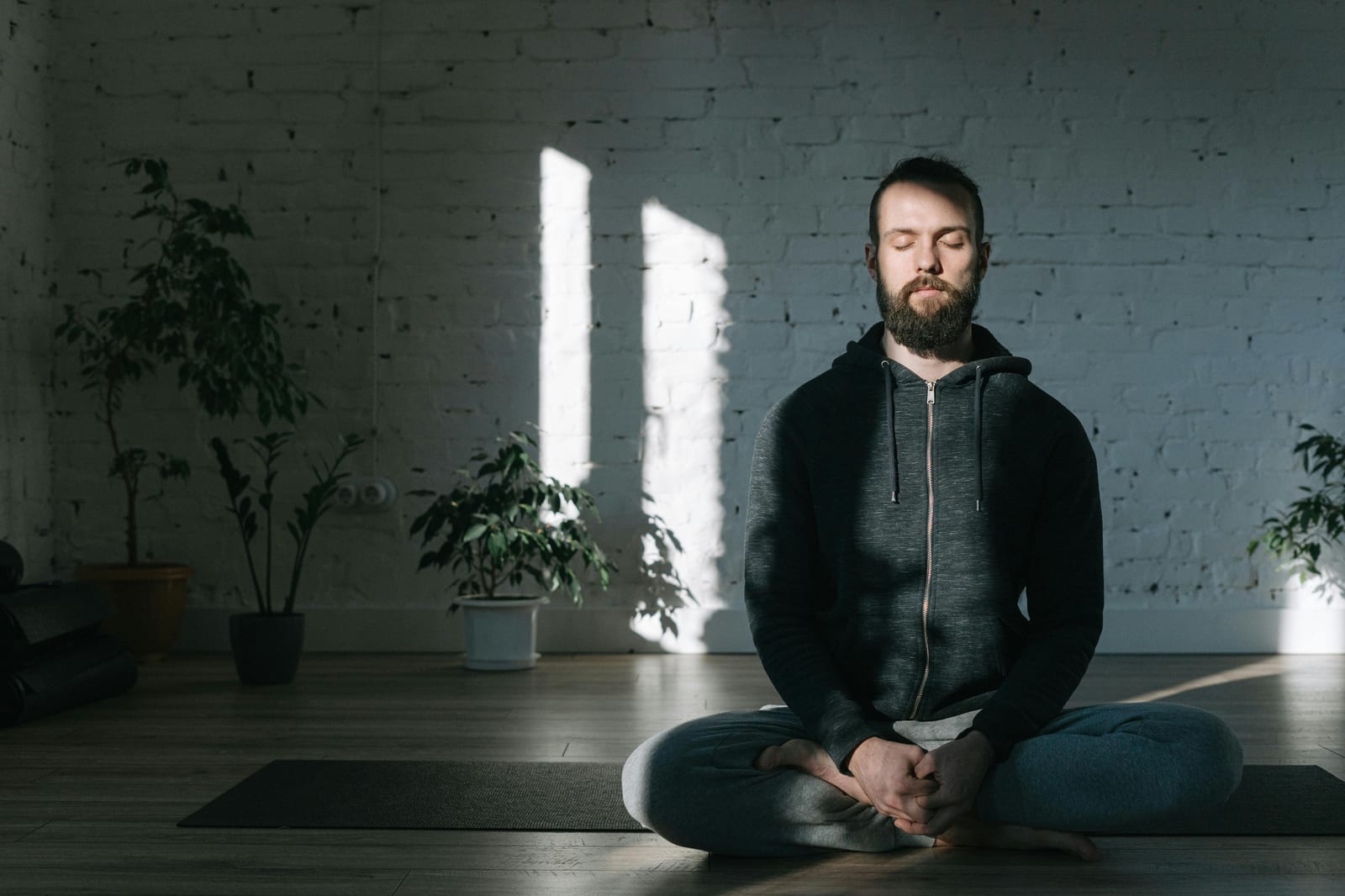 Muž sedí se zavřenýma očima v meditační pozici v prosté místnosti